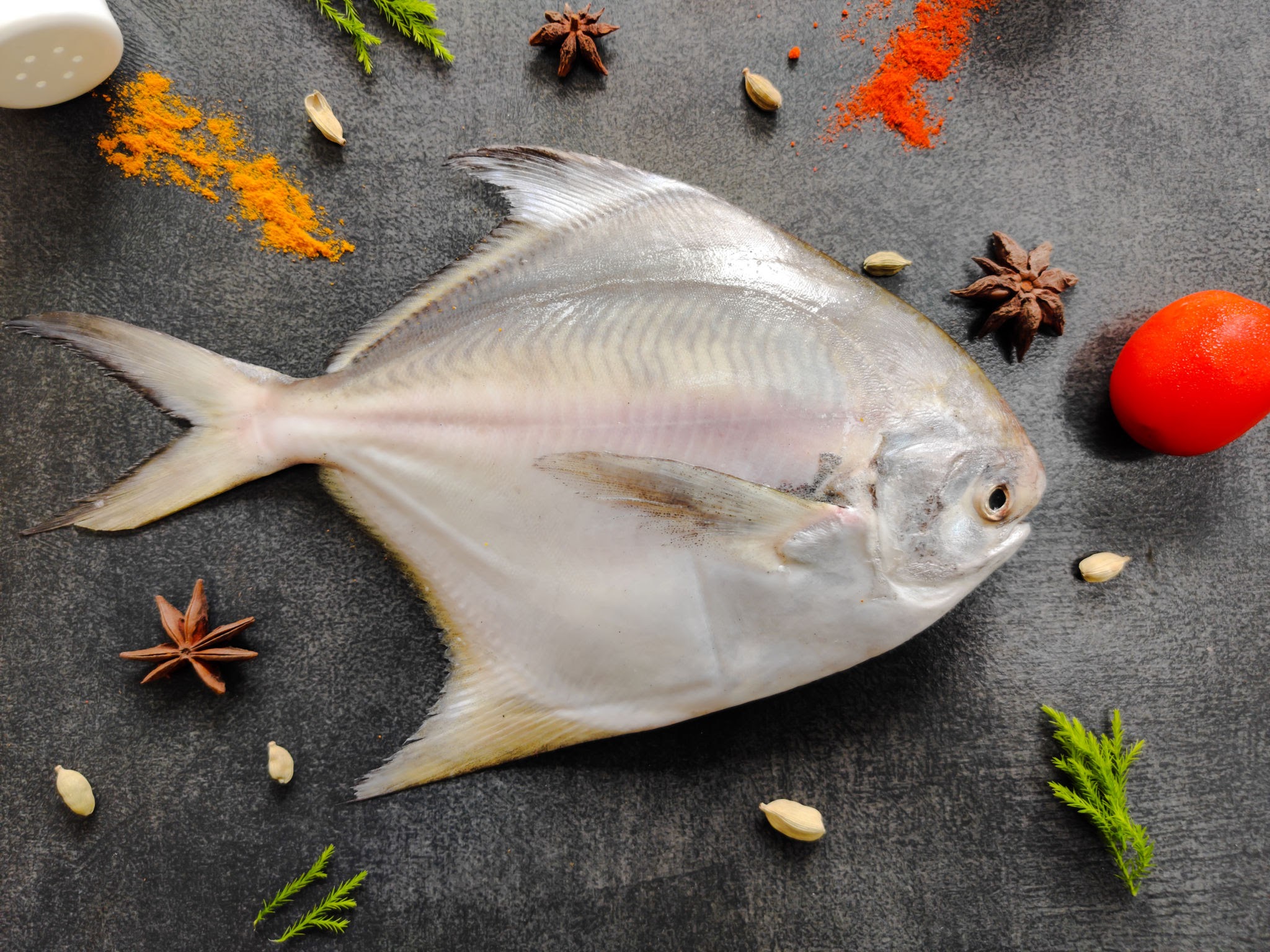 Top view of Silver Pomfret,White Pomfret fish dish cooking with various ingredients. Fresh raw fish decorated on a black background.Selective focus.